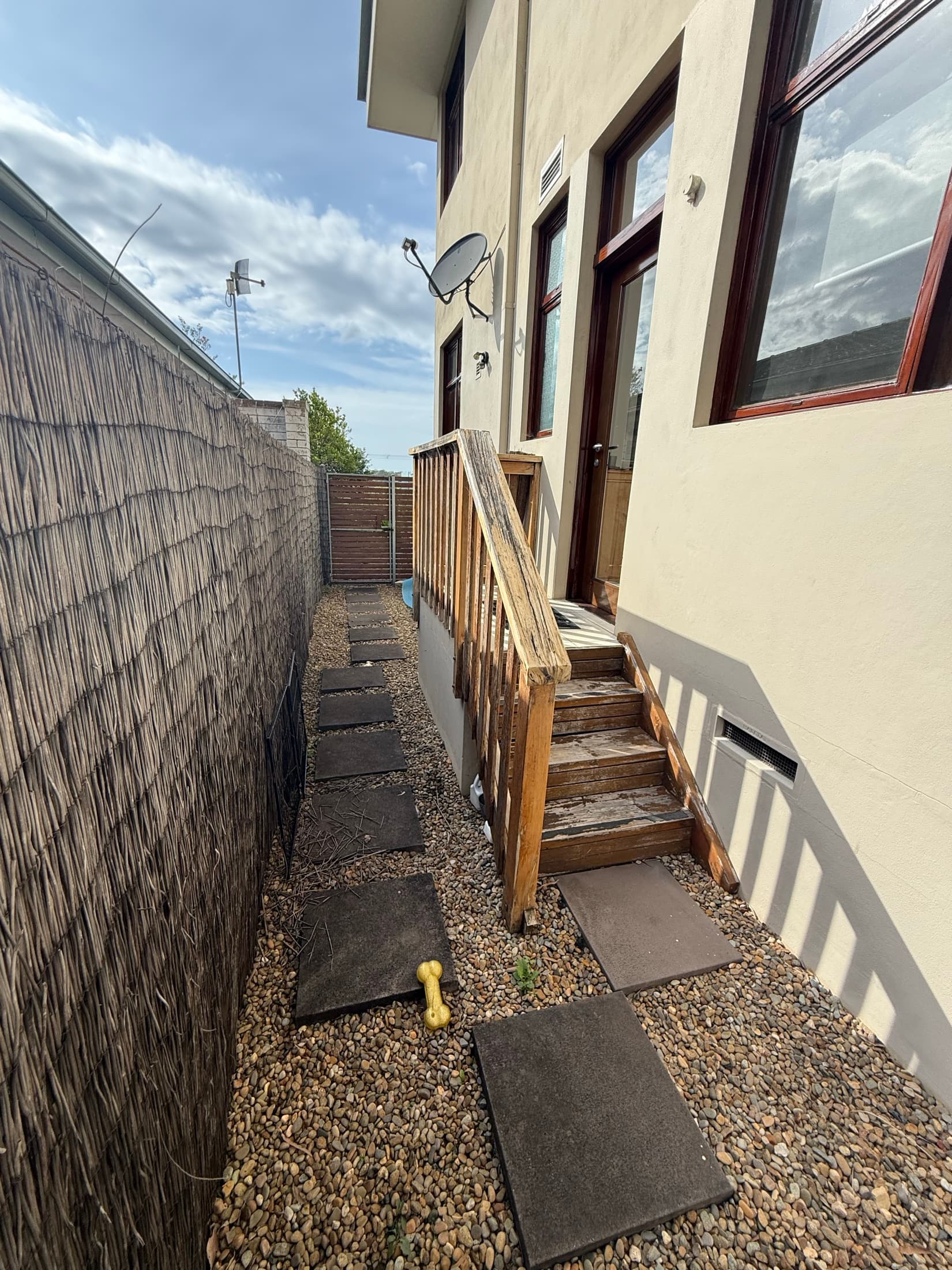 The side passage before the works, loose pavers against a brush fence and worn timber steps